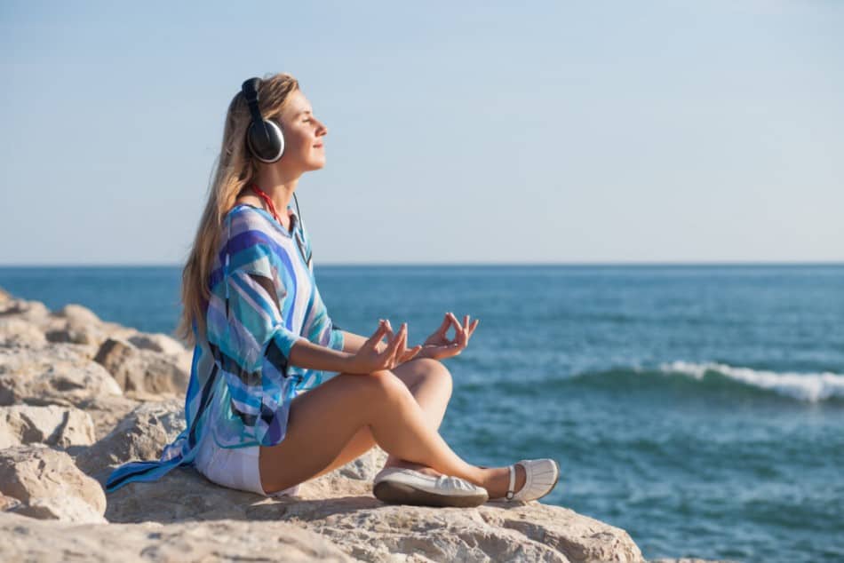 Woman sitting at the beach meditating with headphones on